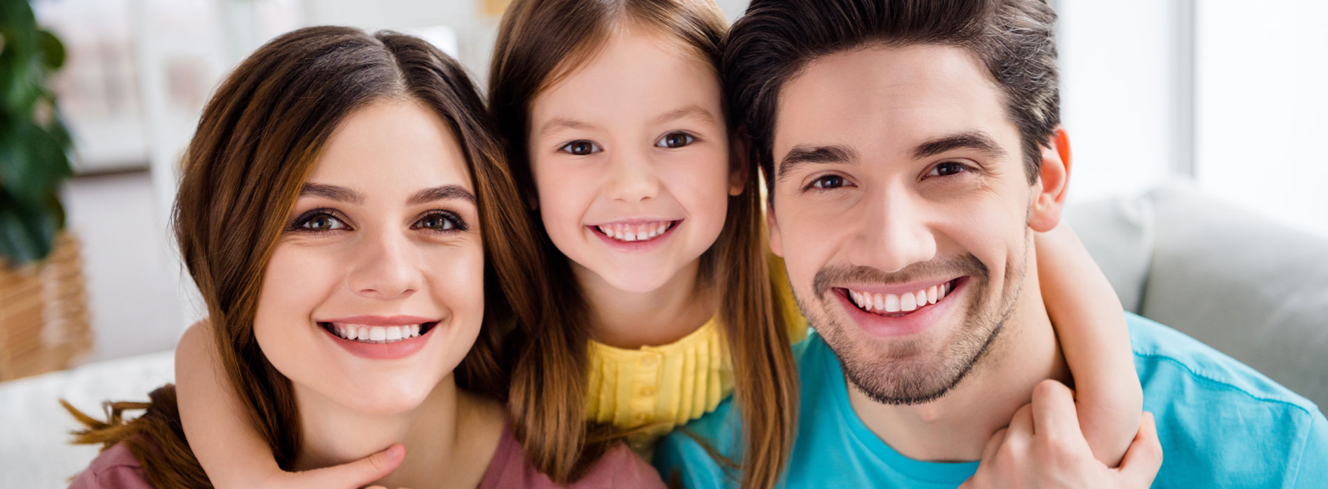 The image shows a family of four with two adults and two children posing for a photograph, with the father holding the younger child and smiling at the camera.