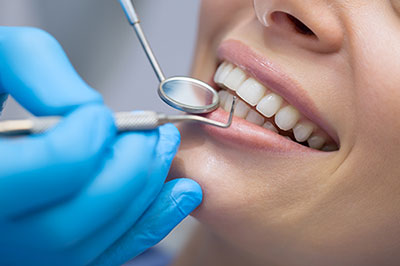 The image shows a person receiving dental care, with a dentist s hands holding tools near their mouth, while they are seated in a dental chair with blue gloves on.