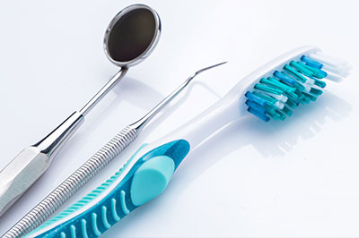 An image featuring dental instruments including a pair of scissors and a toothbrush with blue bristles on a white background.