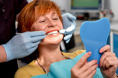 A woman sitting in a dental chair with a blue face mask on her face, receiving dental treatment from a dentist who has a toothbrush in her mouth.