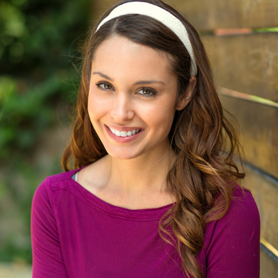 A woman with long brown hair, wearing a purple top, smiles at the camera.