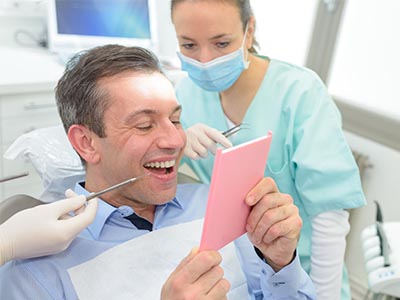 The image shows a man sitting in a dental chair with a tablet displaying a pink card, surrounded by dental professionals who are engaged in their work.