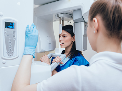 An image depicts two individuals inside a medical facility  one person stands before a large, modern piece of equipment with a digital interface, while another individual stands nearby, observing the scene.