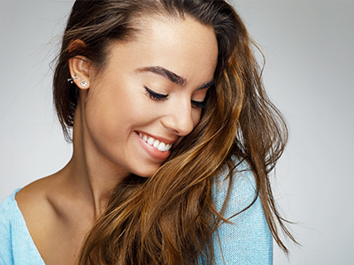 The image shows a woman with long hair smiling at the camera against a plain background.