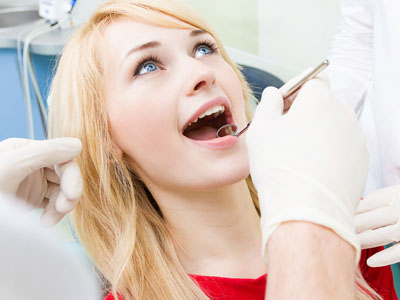 The image shows a woman with her mouth open, receiving dental care from a professional who appears to be performing a procedure on her teeth.